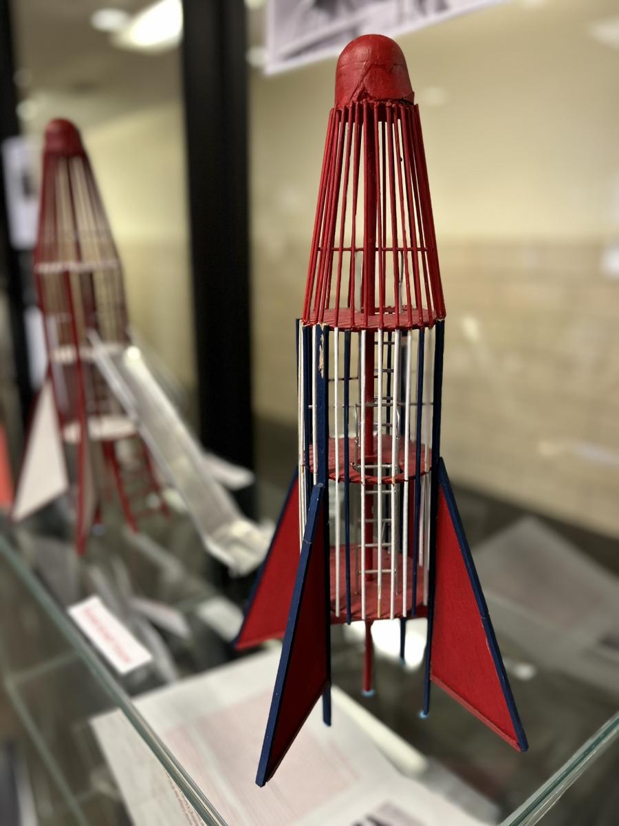 red, white, and blue wooden model of a mid-century playground structure shaped like a rocket, with a metal slide